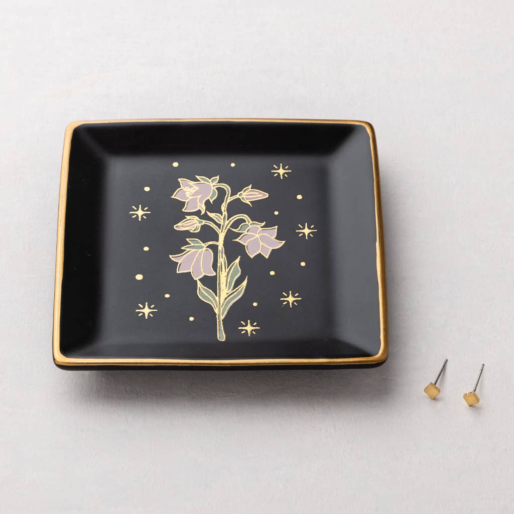 The Jewelry Dish & Stud Earring Set - Flower/Black features a square black ceramic dish with gold trim and a floral center, displayed next to 14k gold-plated stud earrings on a light surface.
